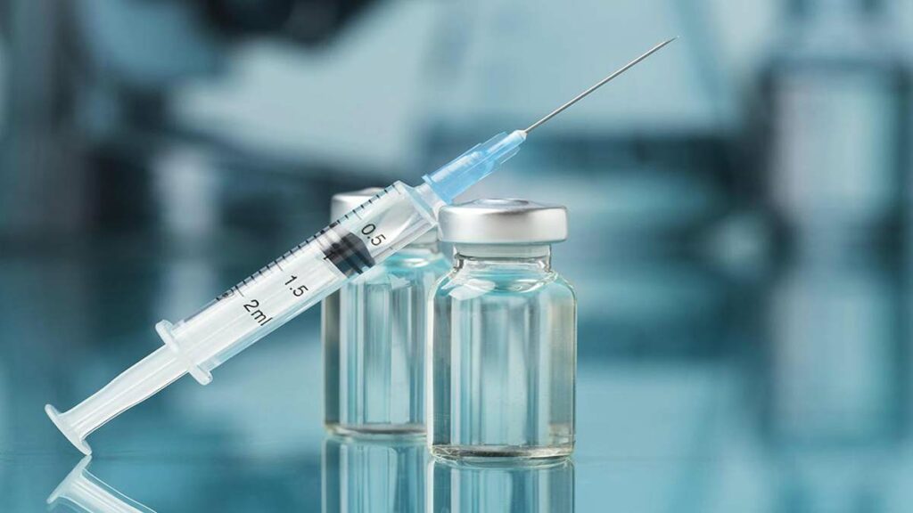 Seringue posée sur deux flacons de vaccin en verre, sur fond médical flouté.