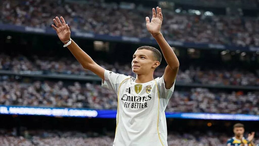 Un jeune marocain en survêtement du Real Madrid salue le public du stade Santiago Bernabéu, sous les applaudissements des joueurs et arbitres.