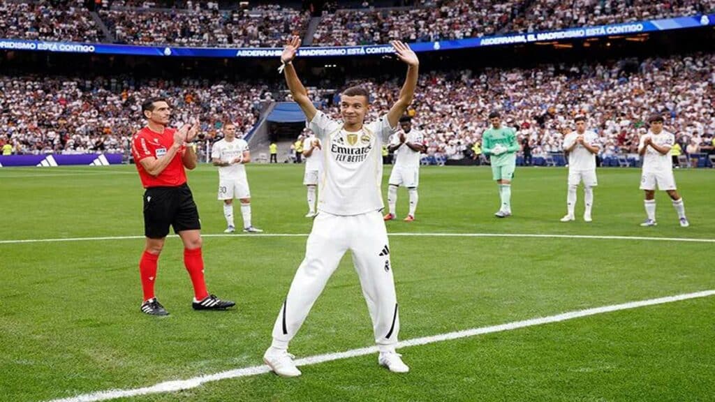 Un jeune marocain en survêtement du Real Madrid salue le public du stade Santiago Bernabéu, sous les applaudissements des joueurs et arbitres.
