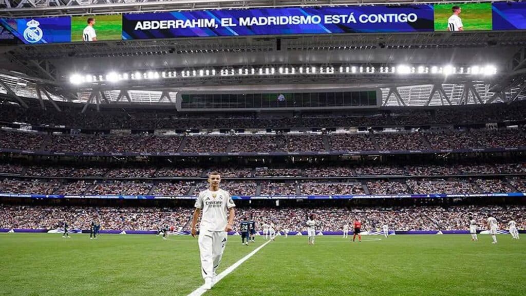 Un jeune marocain en survêtement du Real Madrid salue le public du stade Santiago Bernabéu, sous les applaudissements des joueurs et arbitres.